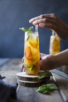 a person holding a glass with some fruit in it on a wooden table next to other people