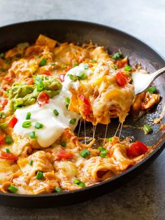 a skillet filled with mexican food on top of a table next to a fork