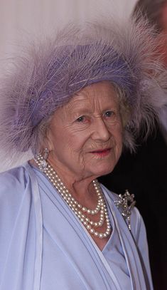 an older woman in a blue dress and pearls is wearing a purple hat with feathers on it