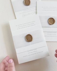 someone is holding some gold buttons in front of two white envelopes with the same design on them