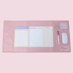 a pink desk mat with a pen, mouse and planner on it in front of a pink background