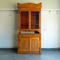 an old wooden china cabinet with glass doors on the top and bottom, against a white wall