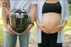 a pregnant woman wearing a helmet next to a man holding a motorcycle helmet in his hands