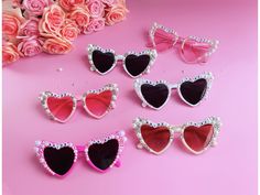 six pairs of heart shaped sunglasses with crystals on the sides and pink roses in the background