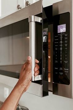 a hand is opening the door to a stainless steel microwave