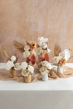 three vases filled with flowers on top of a white table cloth covered tablecloth