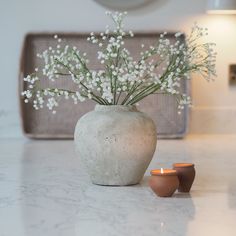 a vase with some flowers in it on a table next to two small candles and a tray