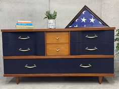 an american flag is on top of a blue dresser with gold handles and brass pulls