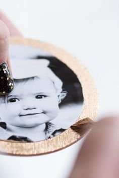 a hand holding a gold and black coaster with a baby's face on it