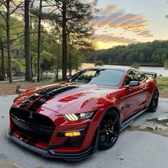 a red sports car parked on the side of a road next to trees and water