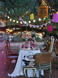 a table set up for a tea party under a tree with birdcages hanging from the branches