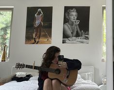 a woman sitting on top of a bed holding a guitar