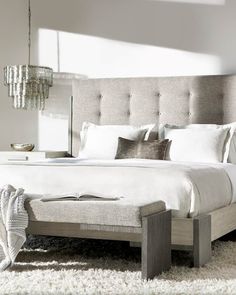 a bed with white sheets and pillows in a bedroom next to a chandelier