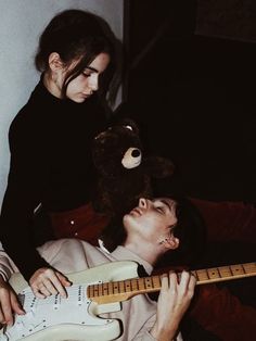 a man laying on top of a bed next to a woman holding an electric guitar