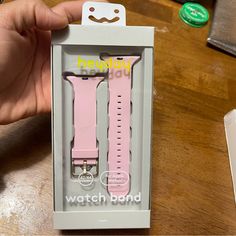 a person holding up a pink watch band in a white box on a wooden table