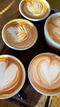 four coffee cups with heart designs on them sitting on a wooden table next to each other