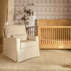 a baby's room with a chair, crib and wallpaper