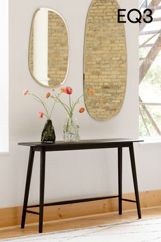 two mirrors on the wall above a table with flowers