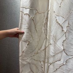 a person is holding up a curtain with white feathers on it and the fabric has been drawn