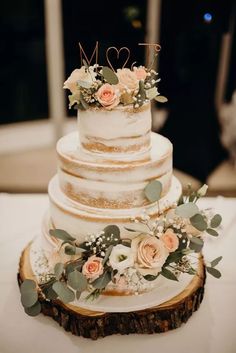 a wedding cake with flowers and greenery is on a wooden slice at the reception table