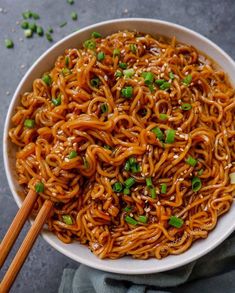 a bowl filled with noodles and chopsticks on top of a gray tablecloth