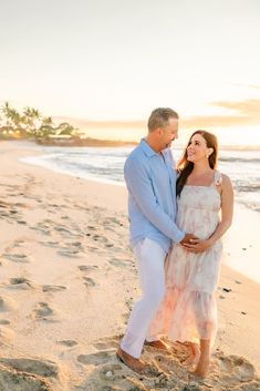 a pregnant couple standing on the beach at sunset