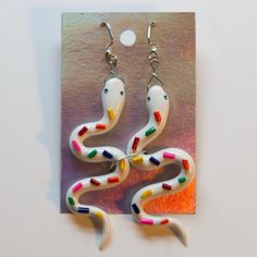 a pair of white and multicolored snake shaped earrings on top of a card