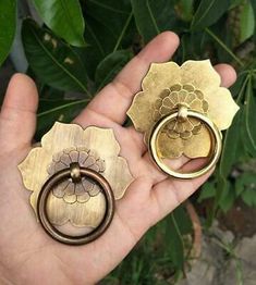 a person holding two gold rings in their hand and another one with a flower on it