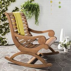 a wooden rocking chair sitting on top of a stone floor next to a potted plant