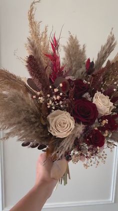 a person holding a bouquet of flowers in their hand with feathers on the bottom and red, white, and brown colors