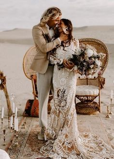 a bride and groom standing in front of a desert backdrop with candles, flowers and an old wicker chair