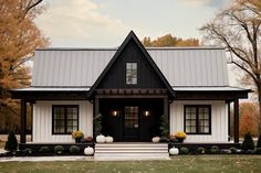 a black and white house with pumpkins on the front porch, and trees in the background