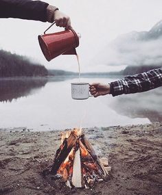 a person holding a cup over a campfire