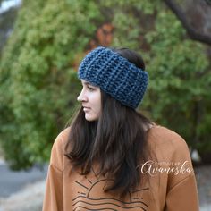 a woman wearing a blue knitted headband in front of some trees and bushes