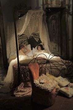 two women laying in bed with an old fashioned canopy over the headboard and foot board