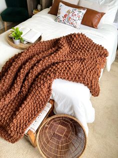 a bed with a brown blanket on top of it next to a wicker basket