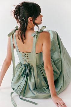 a woman sitting on the ground wearing a green dress with bow ties around her neck