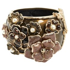 Chanel cuff bracelet in gold metal covered with brown enamel decorated with a large CC in enameled metal on one side and a large floral pattern in glass paste decorated with white rhinestones and fancy pearls, magnetic closure lined with a hook and a safety chain with carabiner, interior lined with quilted black satin. Height of the bracelet 4.65 cm (excluding floral pattern), internal diameter 5.75 cm, dimensions of the CC 4.5 x 3.5 cm, dimensions of the floral pattern 10 x 6 cm. The cuff is in excellent condition and is an exceptional piece, divine on the wrist. Chanel Cuff Bracelet, Chanel Cuff, Satin Noir, Chanel Haute Couture, Safety Chain, Bracelet Cuff, White Rhinestone, Pearl Diamond, Magnetic Closure