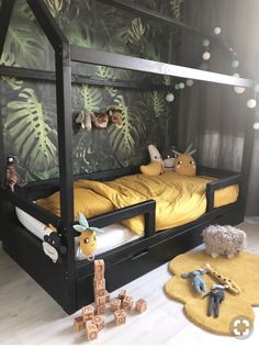 a child's bed with yellow sheets and stuffed animals on the floor next to it