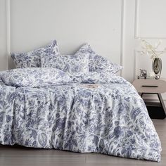 a bed with blue and white comforters in a room next to a nightstand on a wooden floor