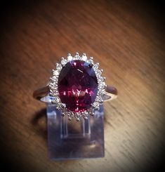 a ring with a large pink stone surrounded by small white diamonds on a wooden surface