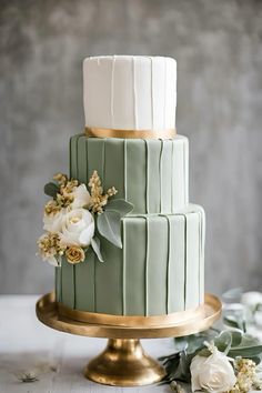 a three tiered green and white wedding cake with flowers on the top, sitting on a gold pedestal