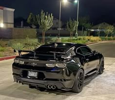 a black sports car parked in front of a parking lot at night with its lights on