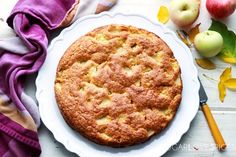 an apple pie sitting on top of a white plate next to apples and a purple towel