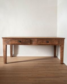 a wooden table sitting on top of a hard wood floor next to a white wall