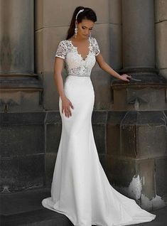 a woman in a white wedding dress leaning against a stone wall with her hand on the ground