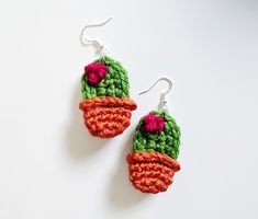 crocheted cactus earrings with pink and green flowers on them, hanging from silver hooks