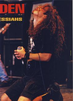 a man with long hair sitting on the ground holding a microphone and looking up at something