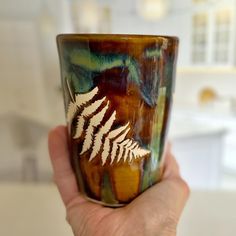 a hand holding a coffee cup with a fern design on the outside, and white leaves on the inside