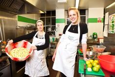 two women standing in a kitchen with food on the counter and one holding a bowl